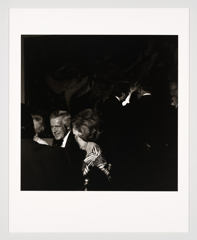A smiling man and a woman sit close together at a dimly lit formal gathering.