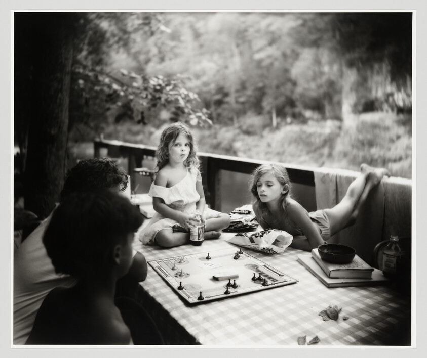Two young girls and two boys play a board game at a picnic table by the water.