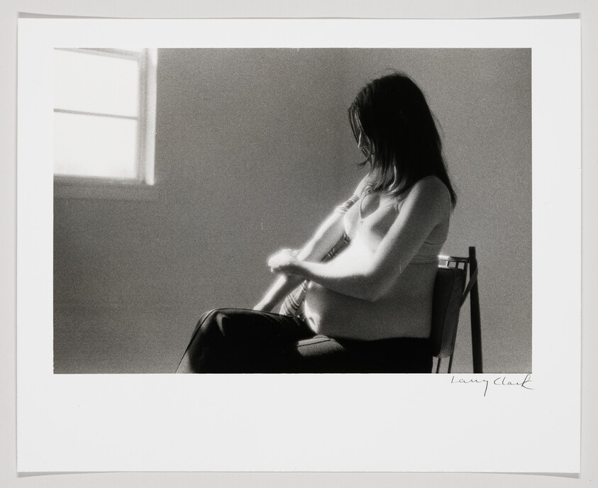 Pregnant woman sitting on a chair by a window gently holding her belly.