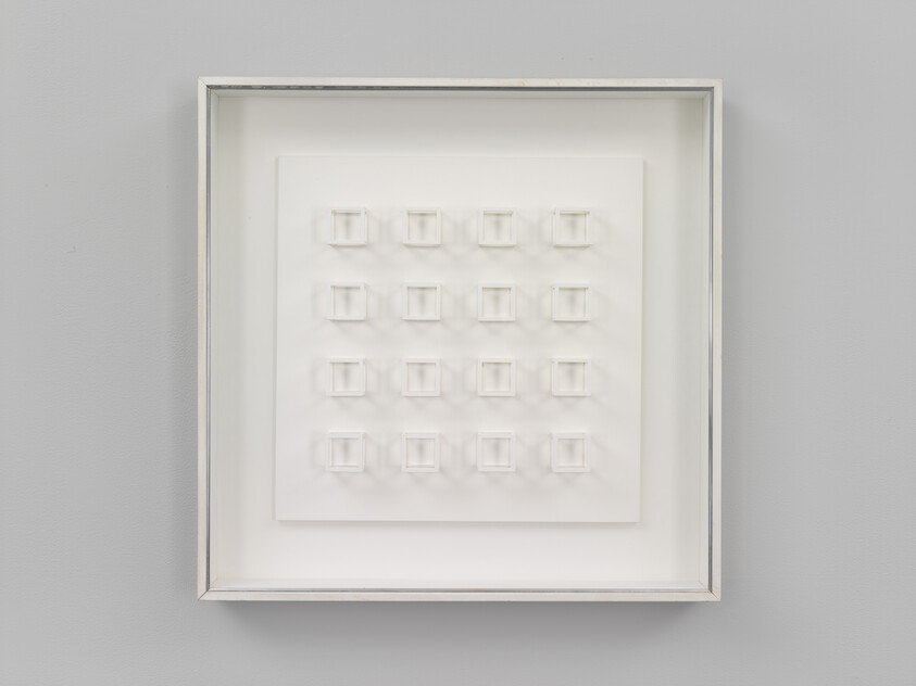 A framed white relief panel shows a 5 by 5 grid of small raised square boxes on a gray wall.