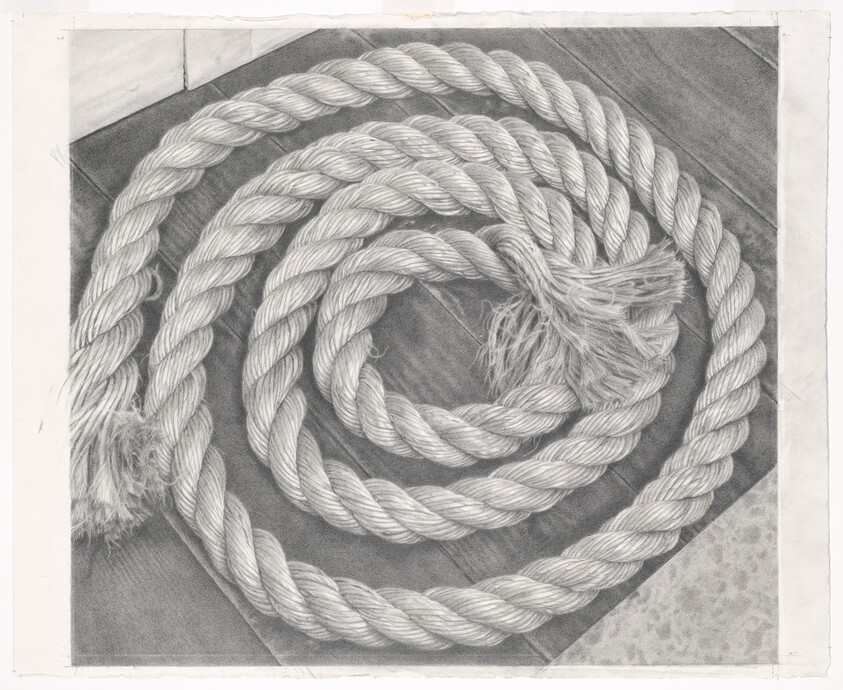 A thick braided rope coiled in a spiral on a wooden floor with frayed ends.