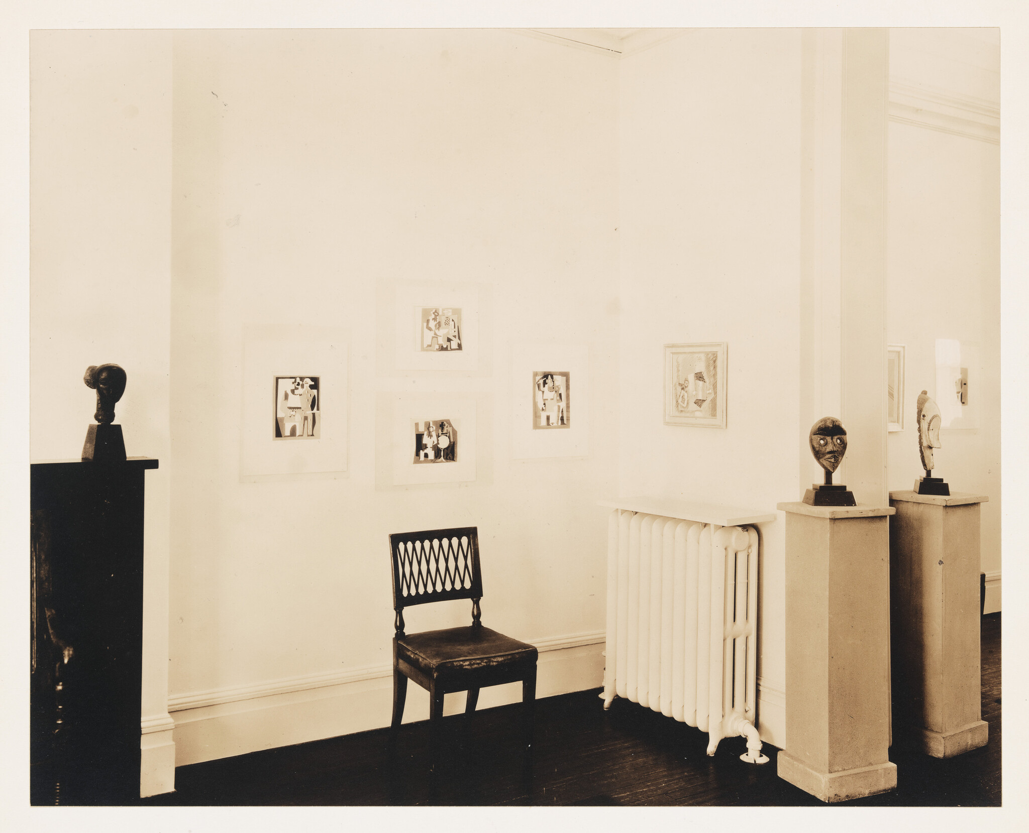 A small gallery room with a wooden chair, radiator, and three sculpted heads on pedestals.