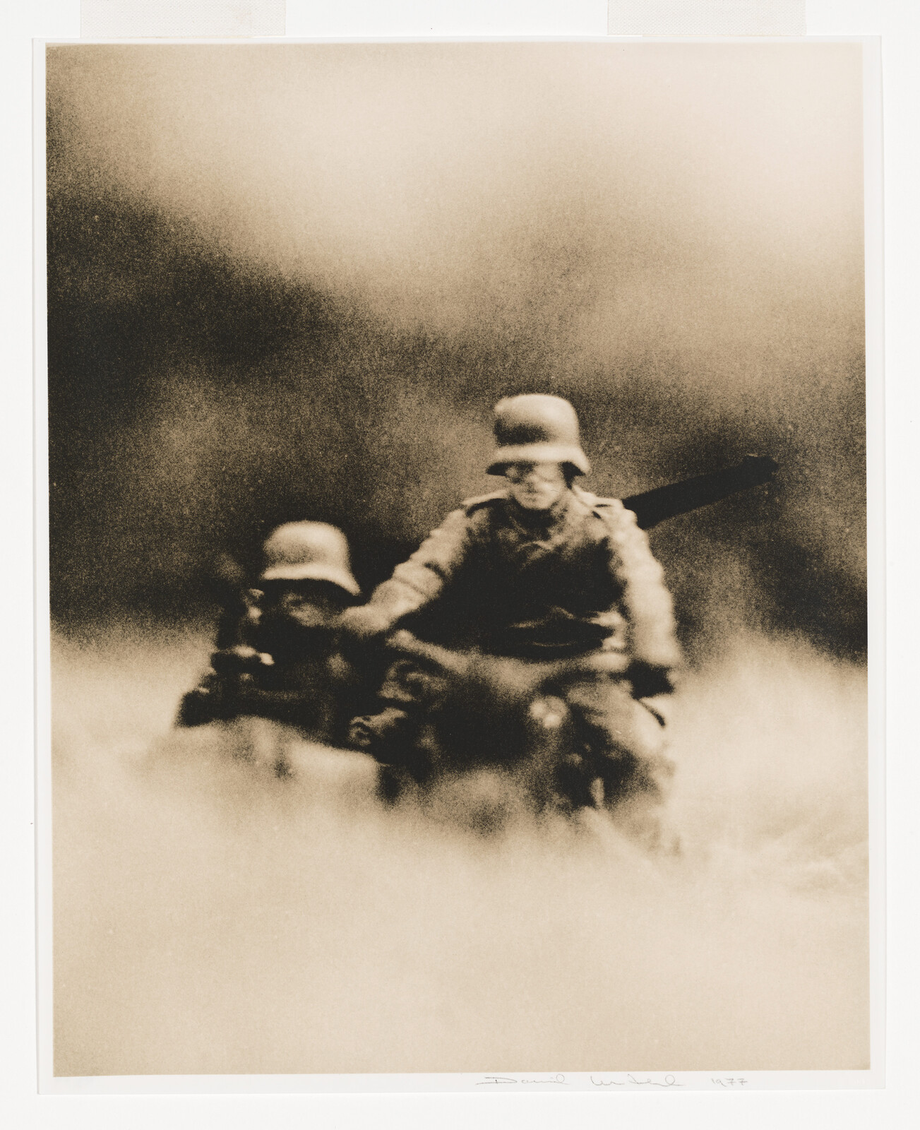 Two soldiers wearing helmets ride a motorcycle through fog and smoke.