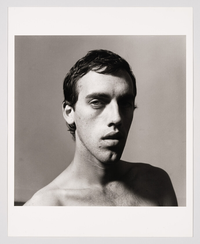 Young shirtless man looking directly at the camera with a neutral, slightly serious expression.