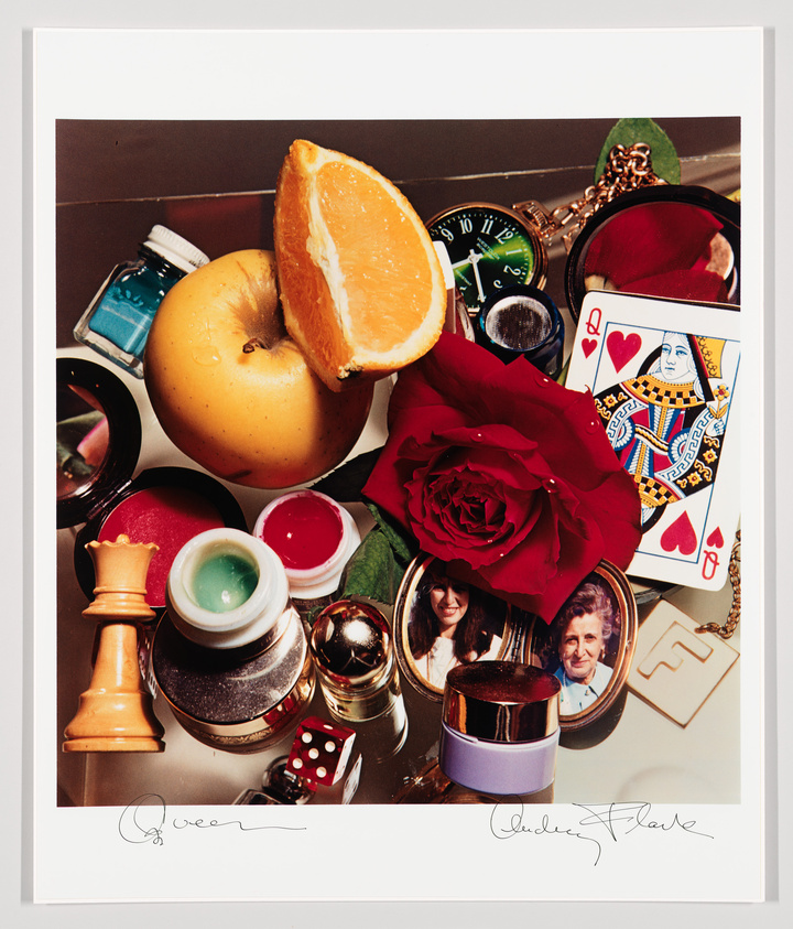 A motley pile of objects, including a red rose, a locket, a chess piece, a sliced orange, and a Queen playing card.