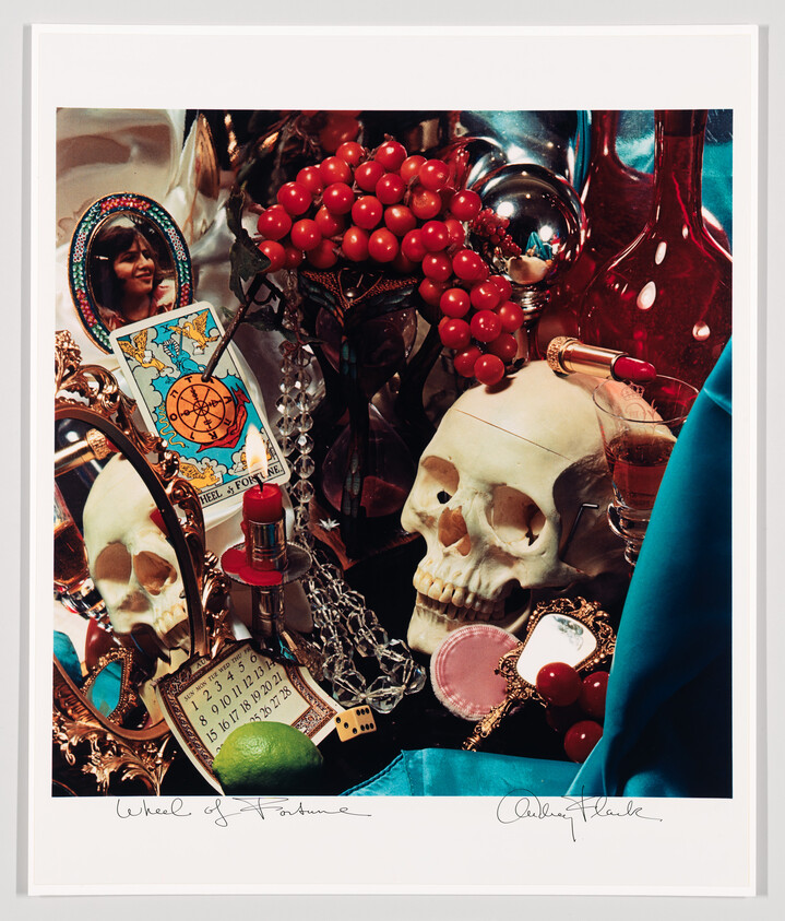 A still life with a skull surrounded by a Wheel of Fortune tarot card, red berries, and makeup.