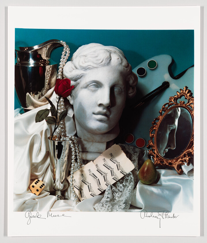 A marble classical bust surrounded by a red rose, pearls, sheet music, mirror, and playing die.