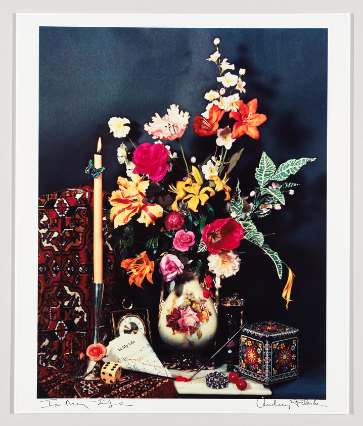 A colorful bouquet of mixed flowers arranged in a decorative vase surrounded by small objects.