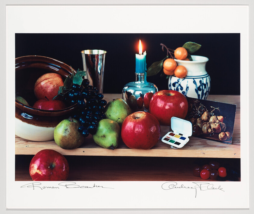 A still-life arrangement of apples, pears, grapes, a lit blue candle, and a small paint palette on a table.