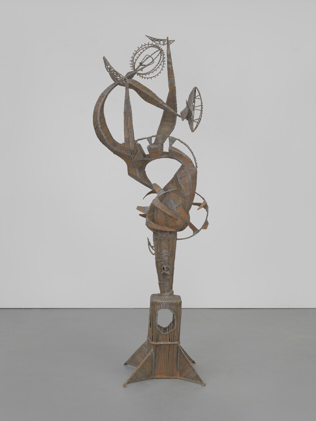 Tall abstract metal sculpture with spiraling arms and circular wheel elements on a square pedestal.