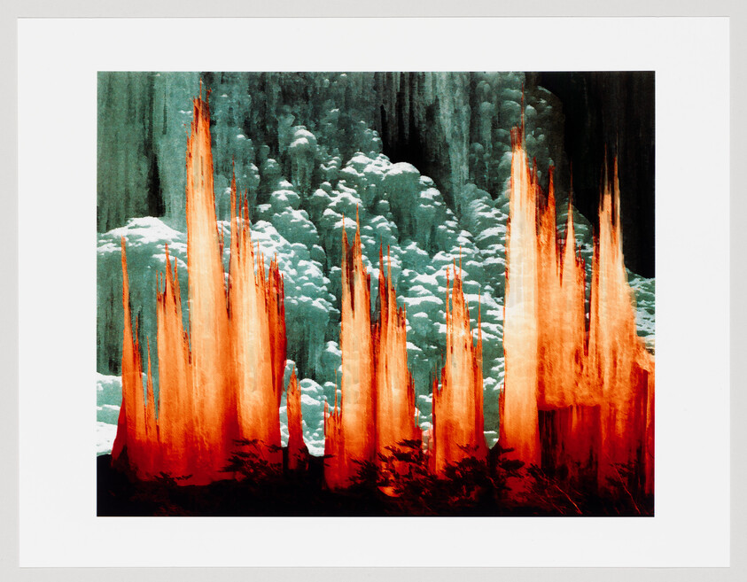 Tall orange flames rise against a blue-green clouded backdrop, silhouetted by dark shapes.