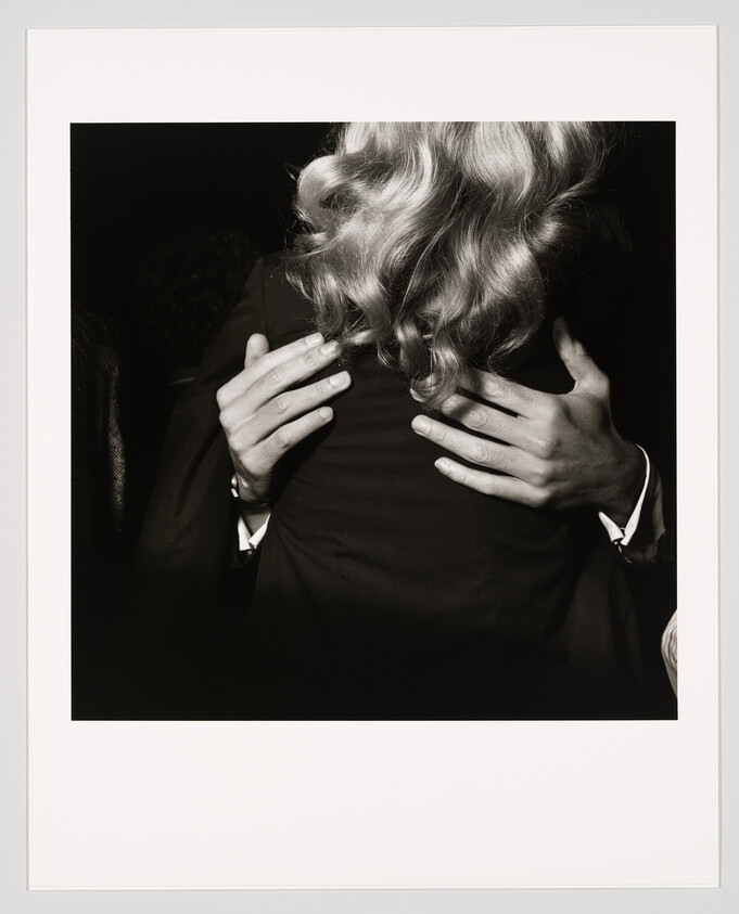 A man in a suit embraces a woman with shoulder-length blonde curls, his hands on her back.