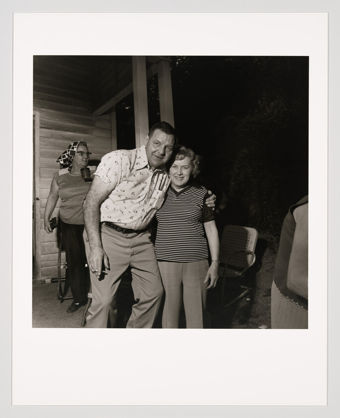 A man with his arm around a smiling woman standing on a porch at night.