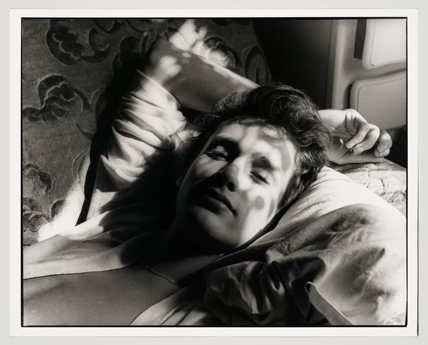 A young person lies on a pillow with dappled sunlight casting patterned shadows across their face.