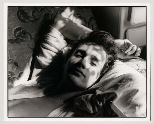 A young person lies on a pillow with dappled sunlight casting patterned shadows across their face.