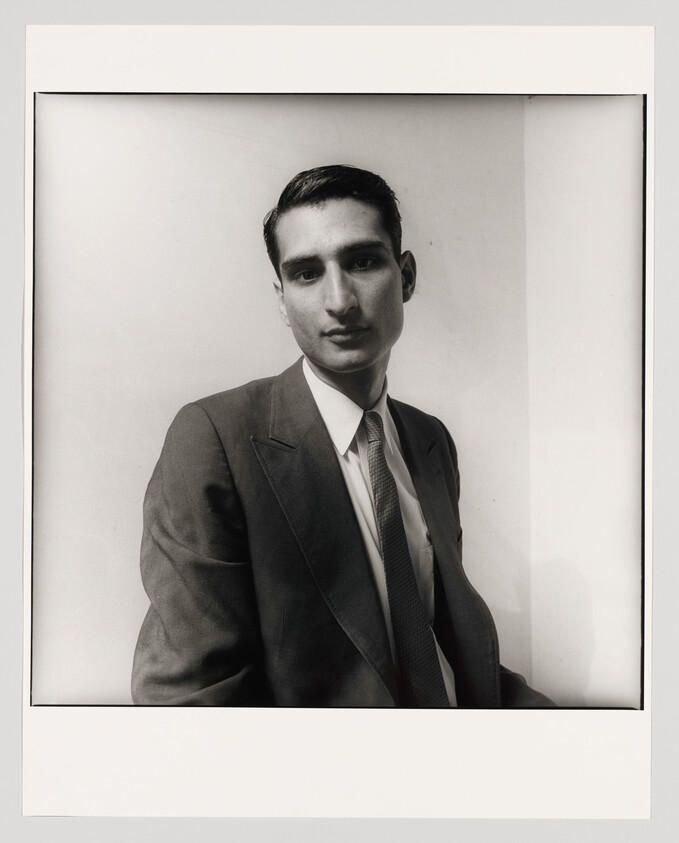 Young man in a suit and tie gazes at the camera with a neutral expression.