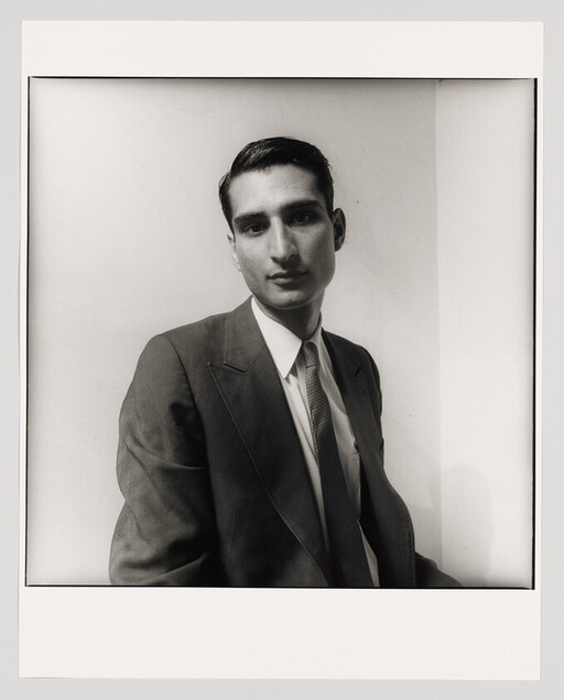 Young man in a suit and tie gazes at the camera with a neutral expression.