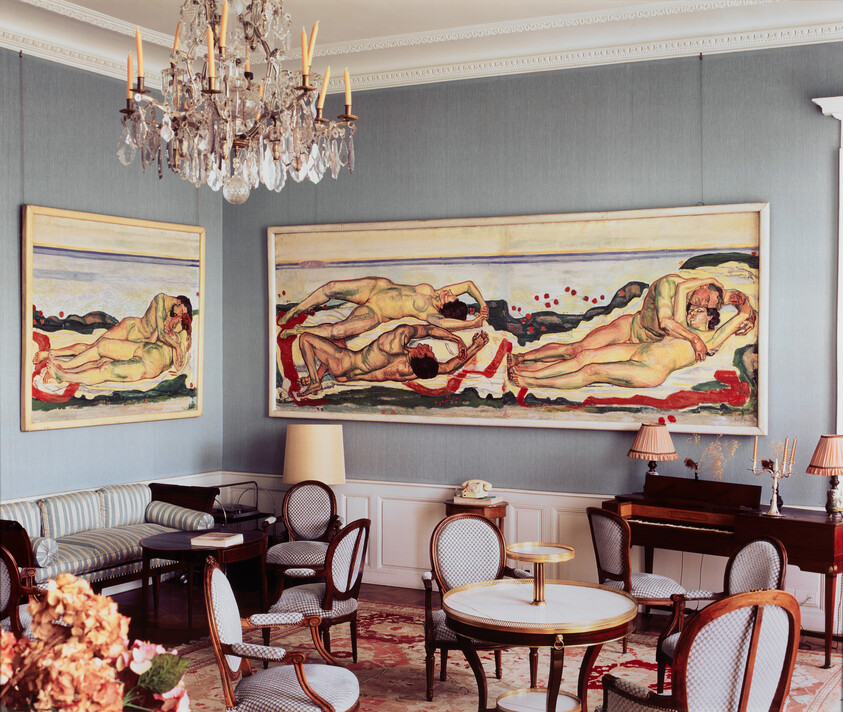 Elegant sitting room with large reclining nude paintings and vintage chandelier above seating area.