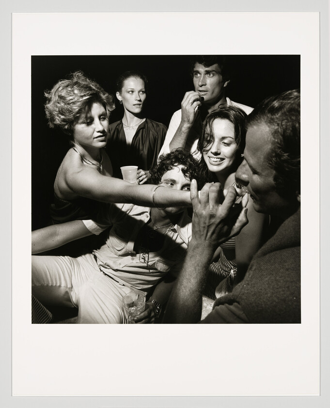 A lively small group of friends crowd together as one man playfully touches another's mouth.