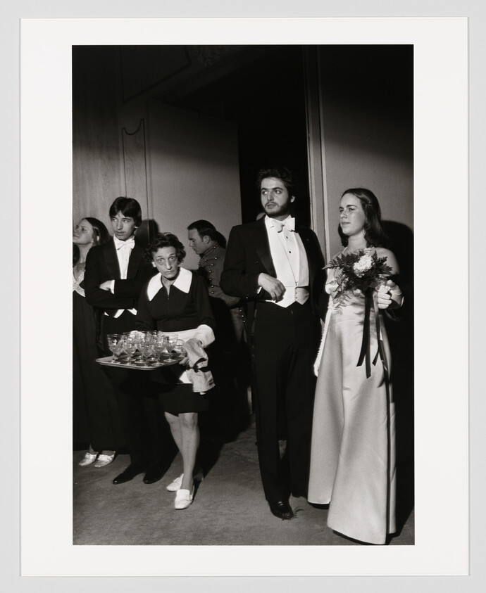 A formally dressed couple stands by a server holding a tray of drinks at an event.