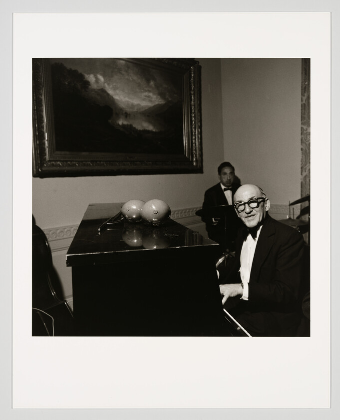 Elderly man in a tuxedo smiles while seated at a grand piano playing for a small band.