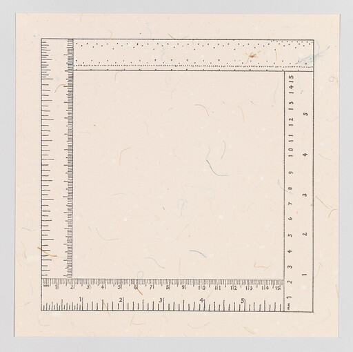 Four rulers form a square measuring frame on speckled off-white paper.