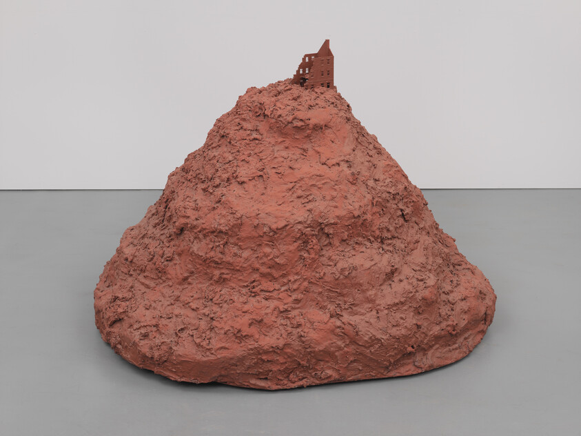 A large rough reddish mound with a small abandoned house perched on its peak in a gallery.