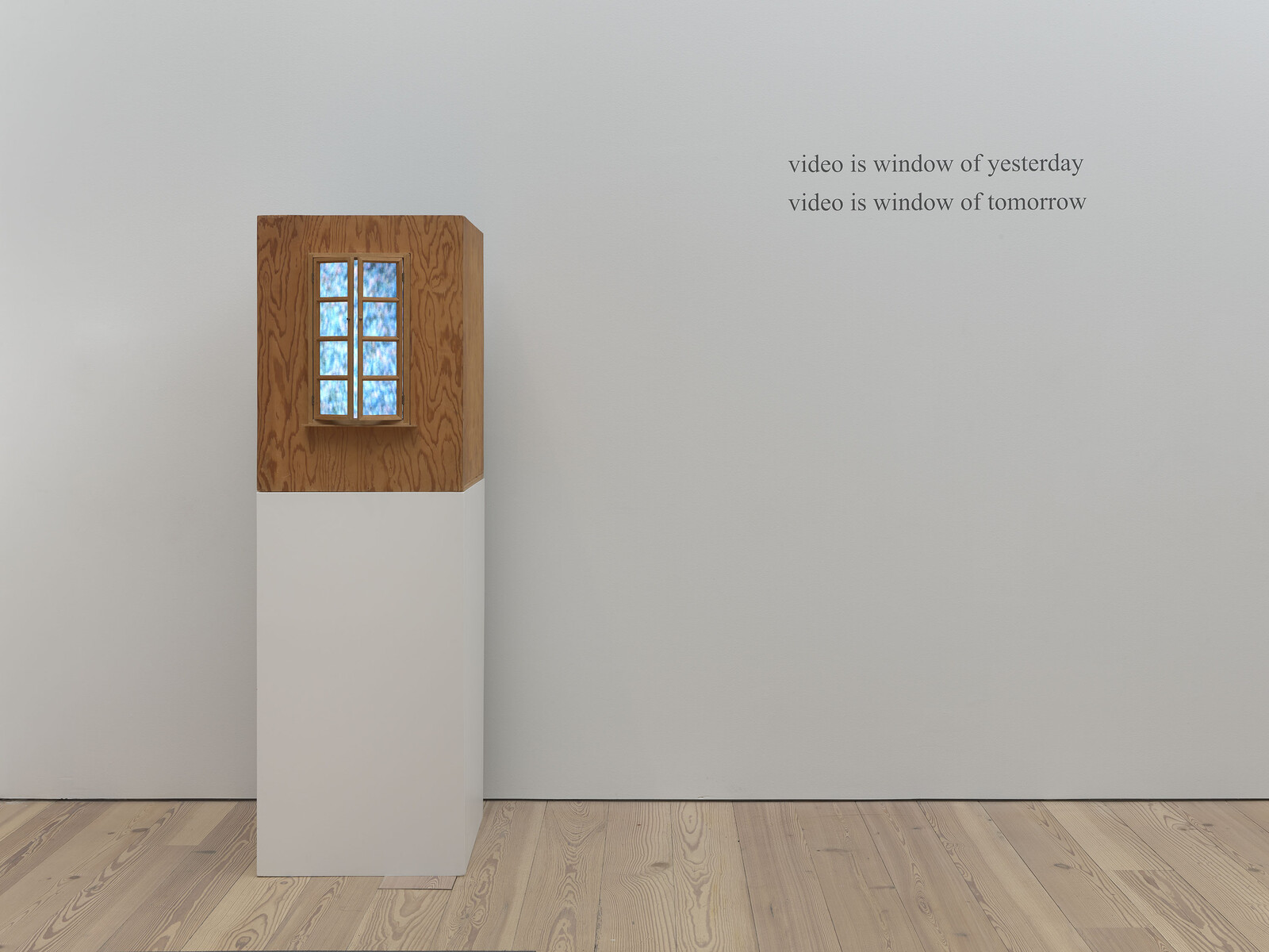 Wooden display box with glowing six-pane window on pedestal beside wall text about video as windows.