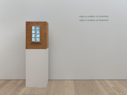 Wooden display box with glowing six-pane window on pedestal beside wall text about video as windows.