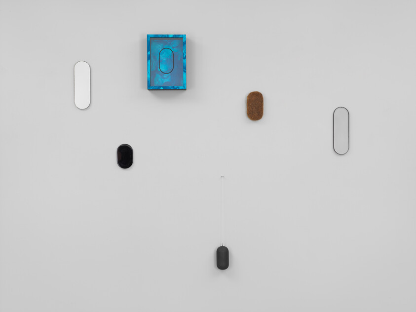 Several small oval-shaped wall objects and a blue box arranged on a white wall, one dangling by a string.