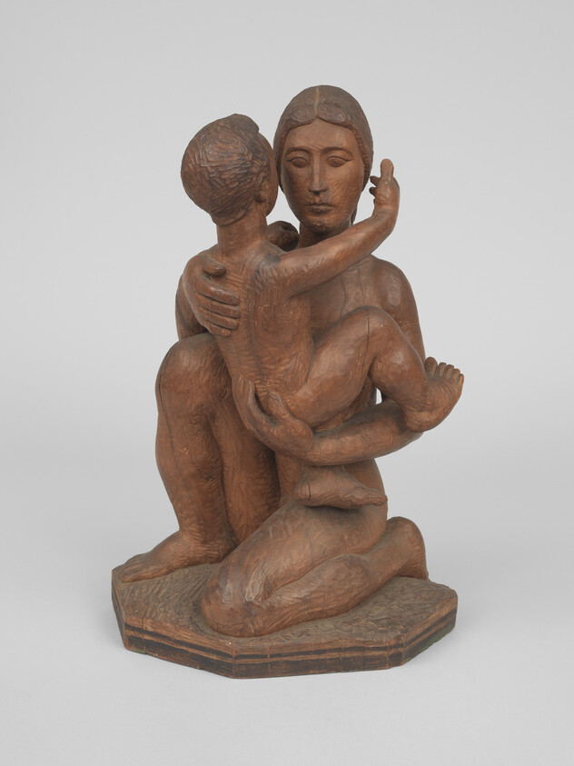 A wooden sculpture of a kneeling mother holding and embracing a child close to her.