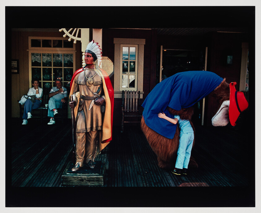 A child hugging a large costumed bear while a statue of a Native American stands nearby.