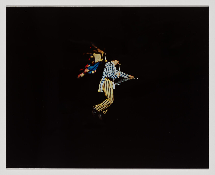 A performer in a checked jacket and striped pants jumps midair holding an umbrella.