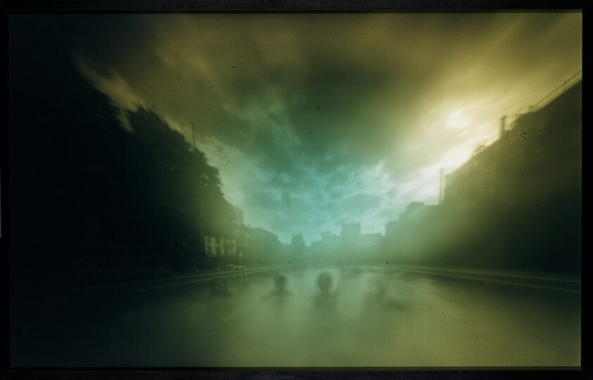 Blurred canal view with buildings and dramatic greenish clouds reflected in calm water.