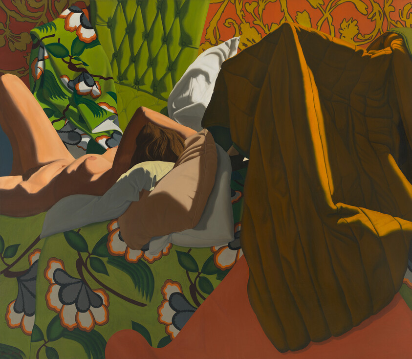 A nude person lies face down on a patterned green sofa, partly covered by pillows and a blanket.