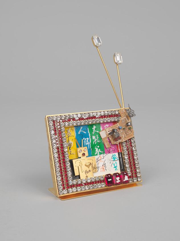 Small jeweled decorative television with antennas, colorful printed panels, and a circuit-board ornament on the frame.