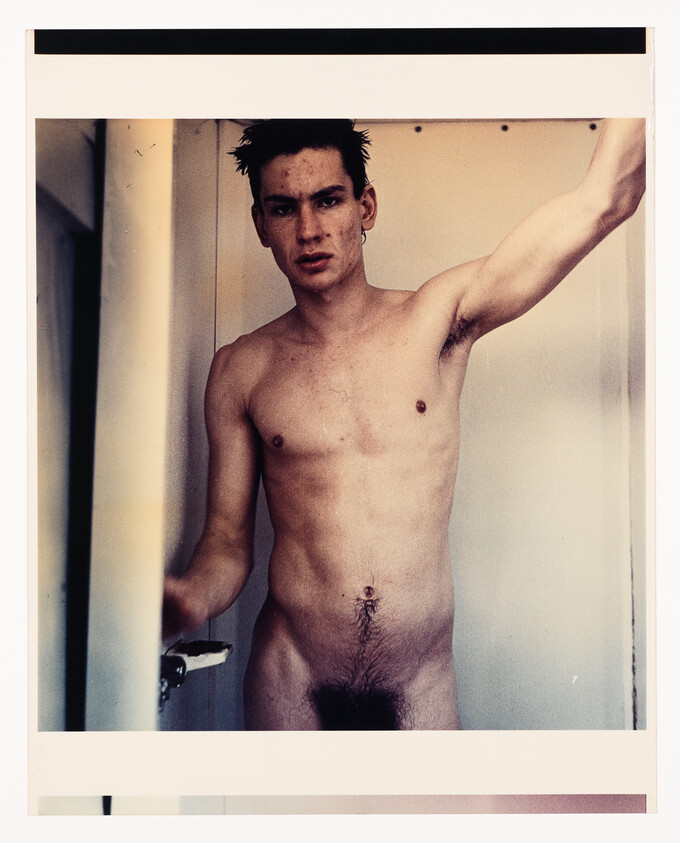 Man standing in a doorway with one arm raised, looking directly at the camera.