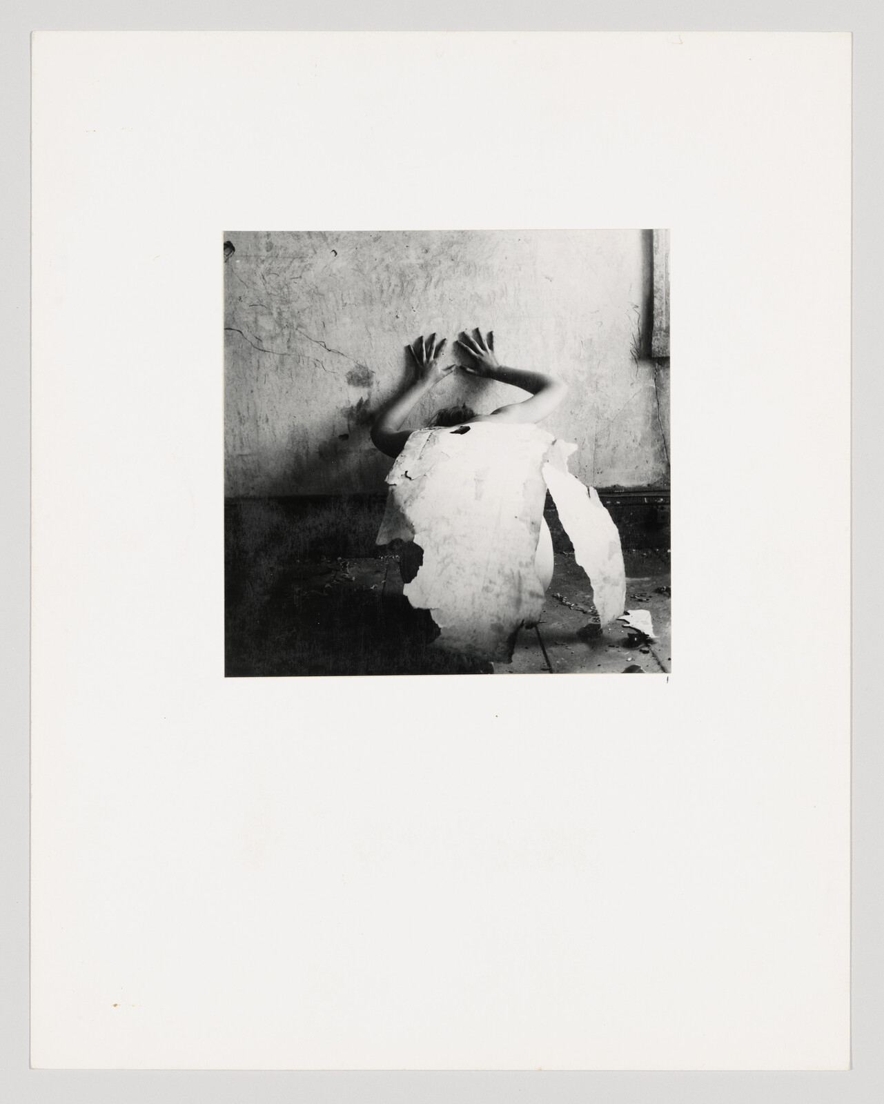 A figure's hands are pushed aganist a wall in a dark and unkept room