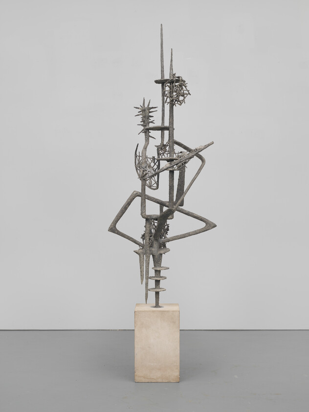 Tall abstract metal sculpture with angular rods and spiky forms mounted on a rectangular stone pedestal.
