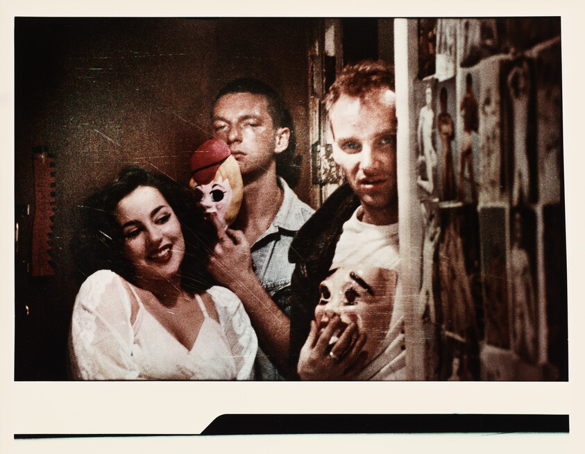 Three people stand close together holding masks, one woman smiling while two men peer from behind.