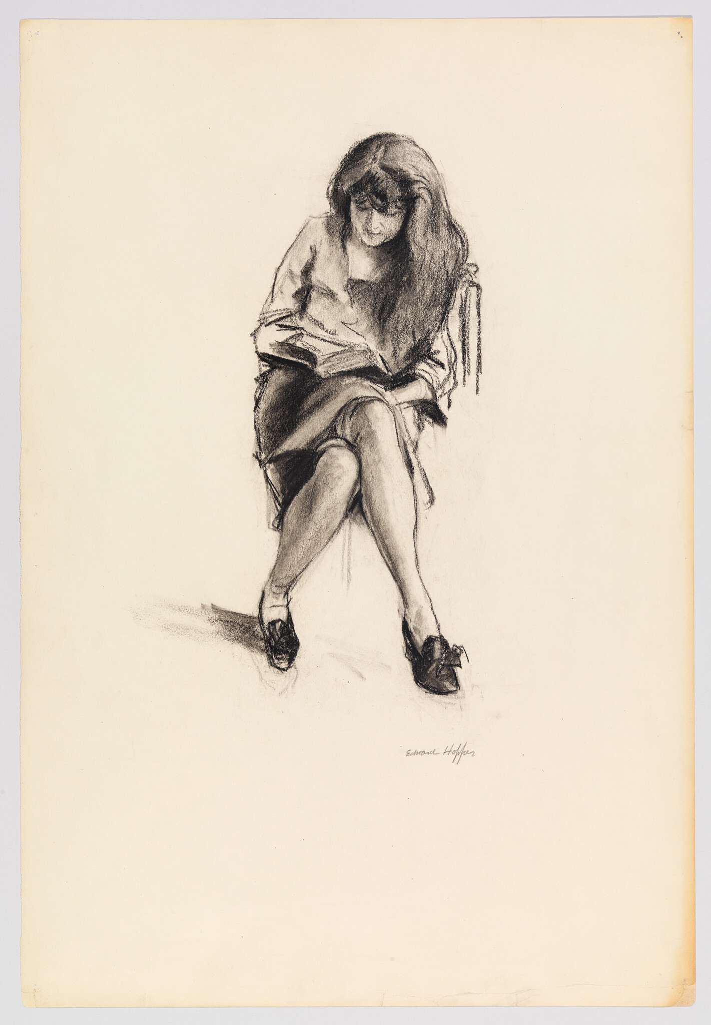 A young woman sitting on a chair with legs crossed, intently reading a book.