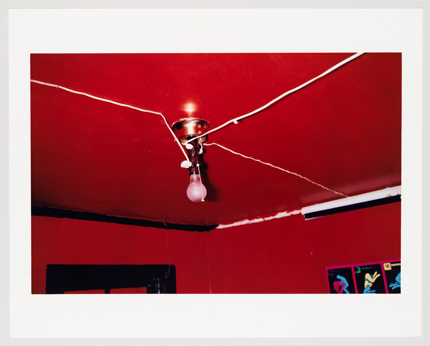 A bare light bulb hangs from the ceiling with exposed wires crisscrossing a red room.