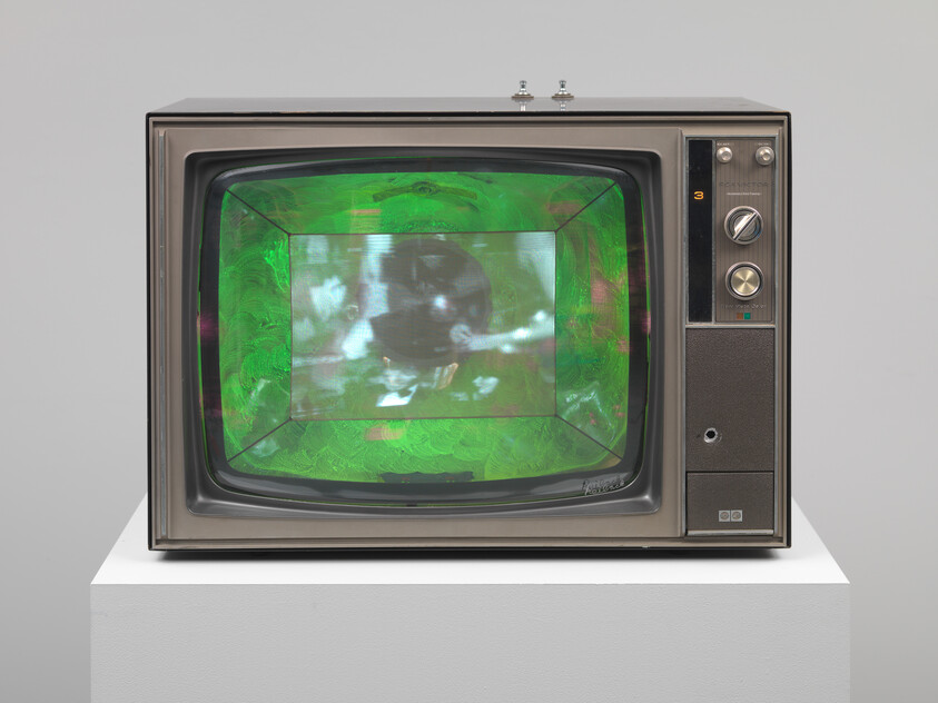 A vintage television sits on a white pedestal showing a green, distorted image on its screen.