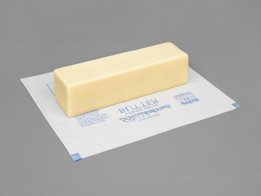A stick of butter sits on a waxed paper wrapper against a gray background.