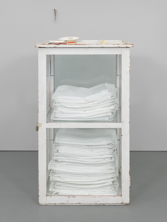 A glass-front cabinet holds neatly folded white linens stacked on two shelves.