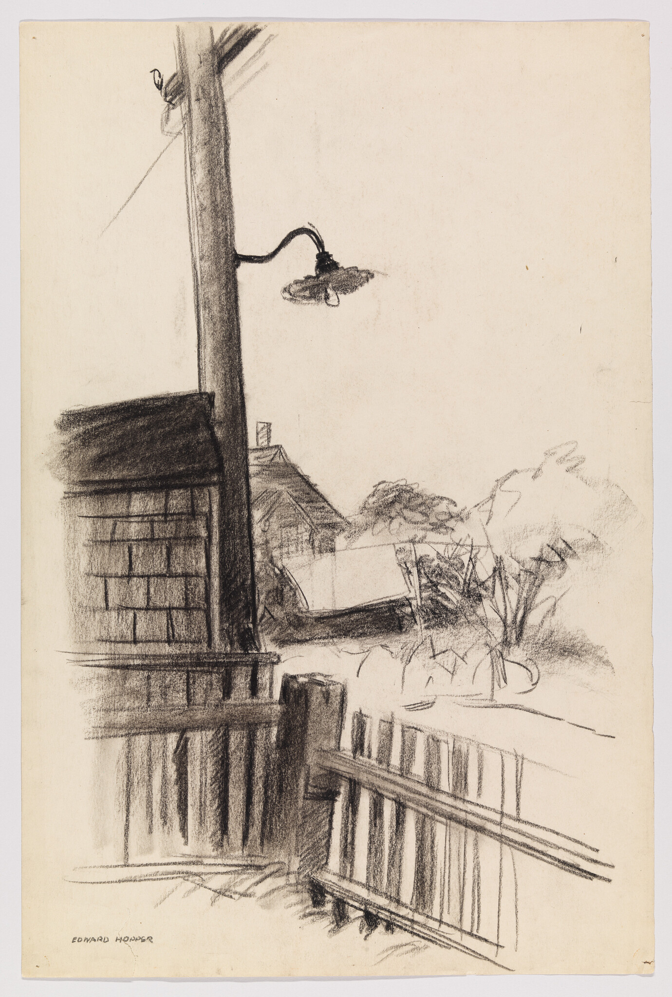 A tall utility pole with a curved streetlamp stands beside a wooden fence and nearby houses.