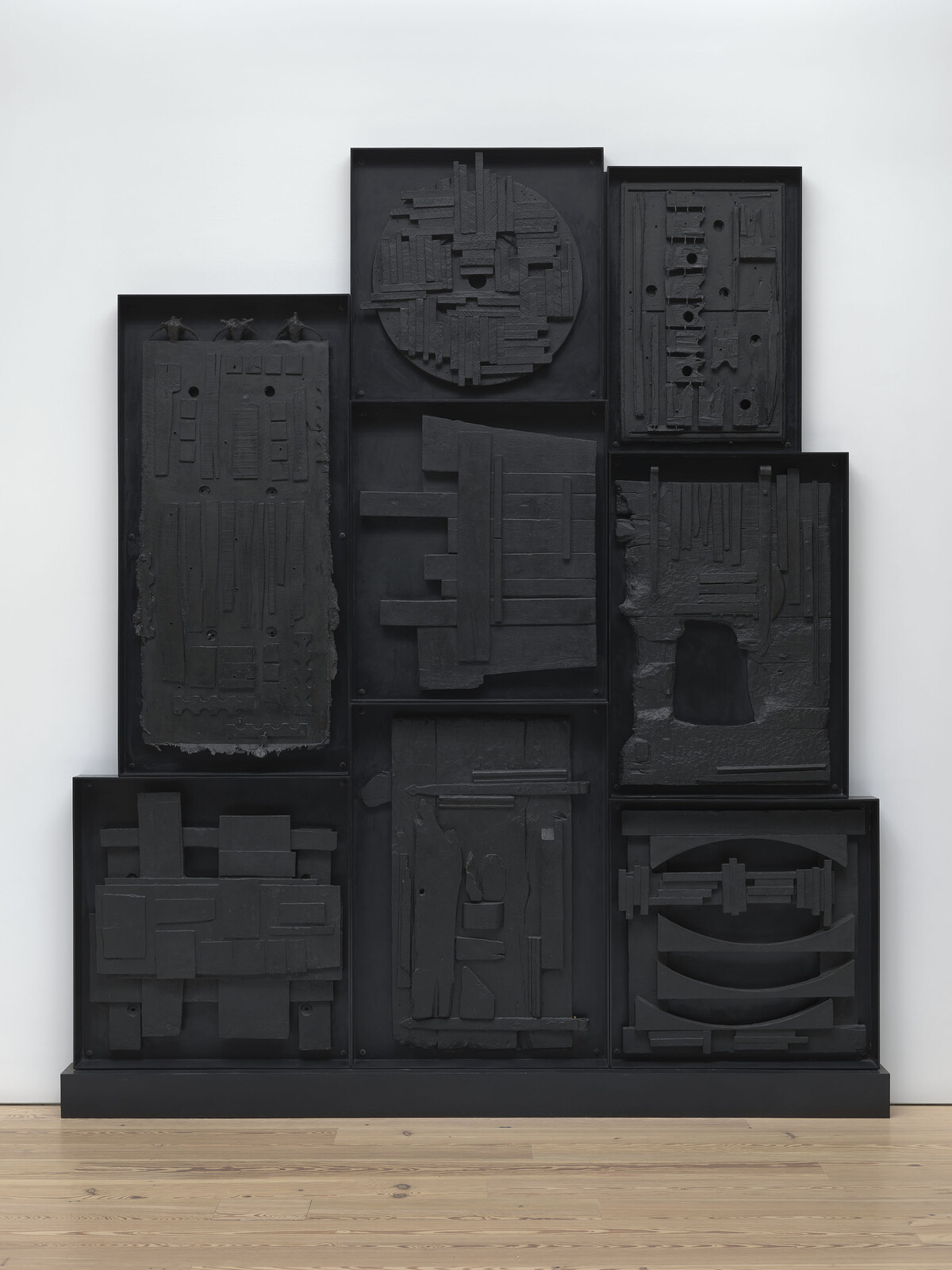 Large black wall sculpture made of nine panels with geometric and textured abstract shapes arranged in a grid.
