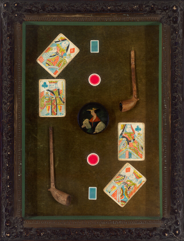 Four playing cards, two wooden pipes, and three game tokens arranged on green felt in a carved frame.