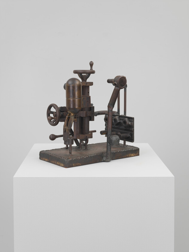 Small rusted metal mechanical sculpture resembling vintage drilling press with gears and levers on pedestal.