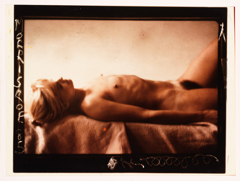 A reclining nude person lies on a cloth-covered surface photographed in warm sepia tones.